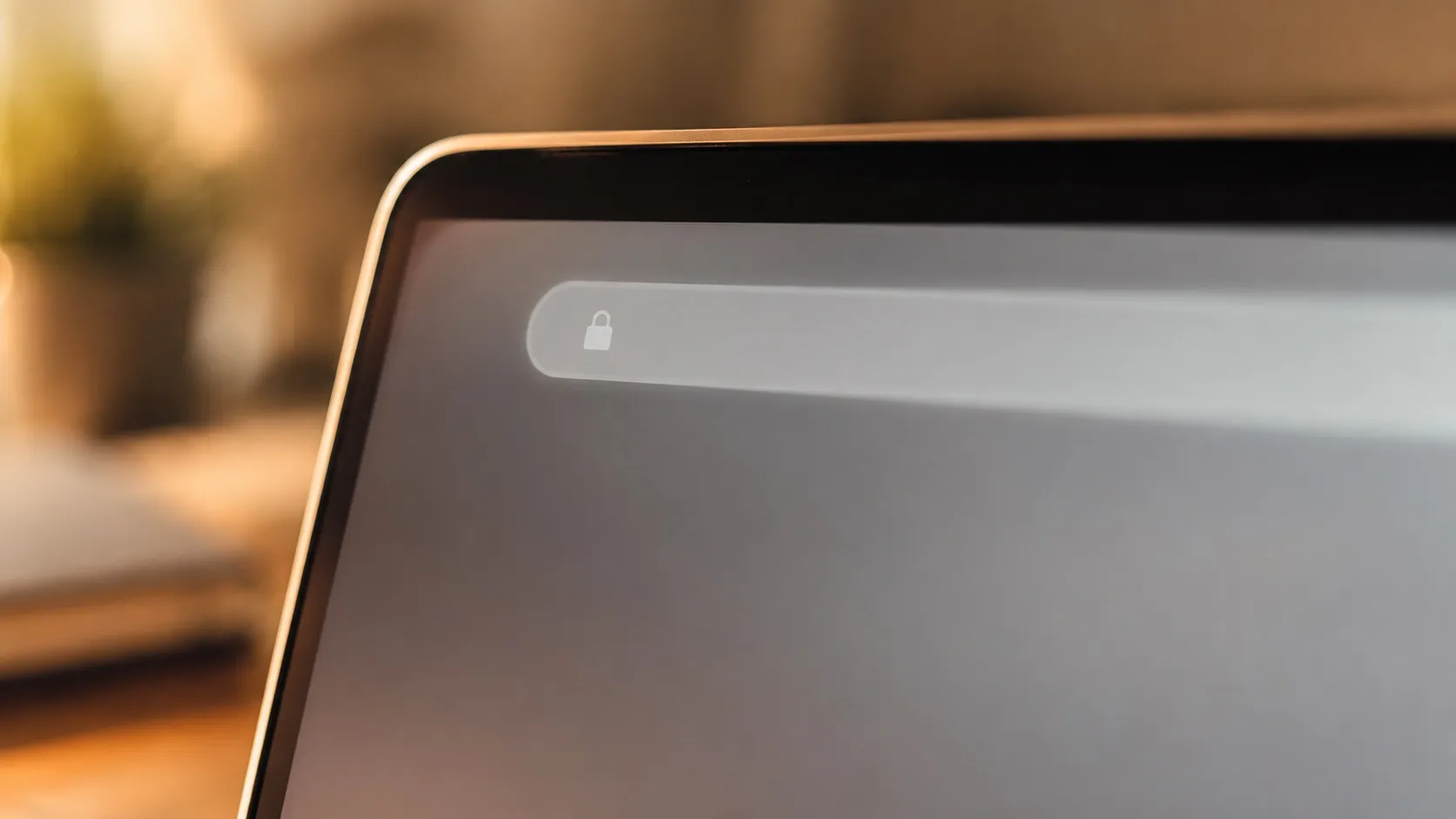 Detailní záběr horní části okna prohlížeče na obrazovce notebooku s rozostřeným zaobleným adresním řádkem a malou ikonou zámku, bez čitelného textu. Zbytek obrazovky a stolu splývá do měkkého rozostření. Snímek symbolizuje webovou adresu neboli URL v prohlížeči.
